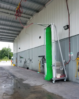 Awash green vertical tower brush installed in a fleet wash bay for cleaning trucks, buses and motorcoaches