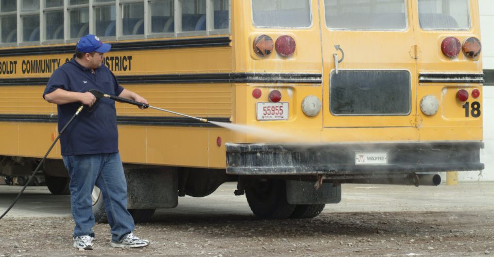 Technician pressure washing a yellow school bus with Enzo's transportation detergents to remove road grime and salt